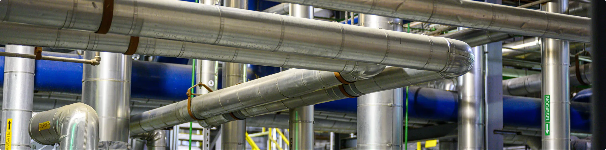 Industrial facility with large metal pipes, ducts, and processing equipment extending through an interior production area.