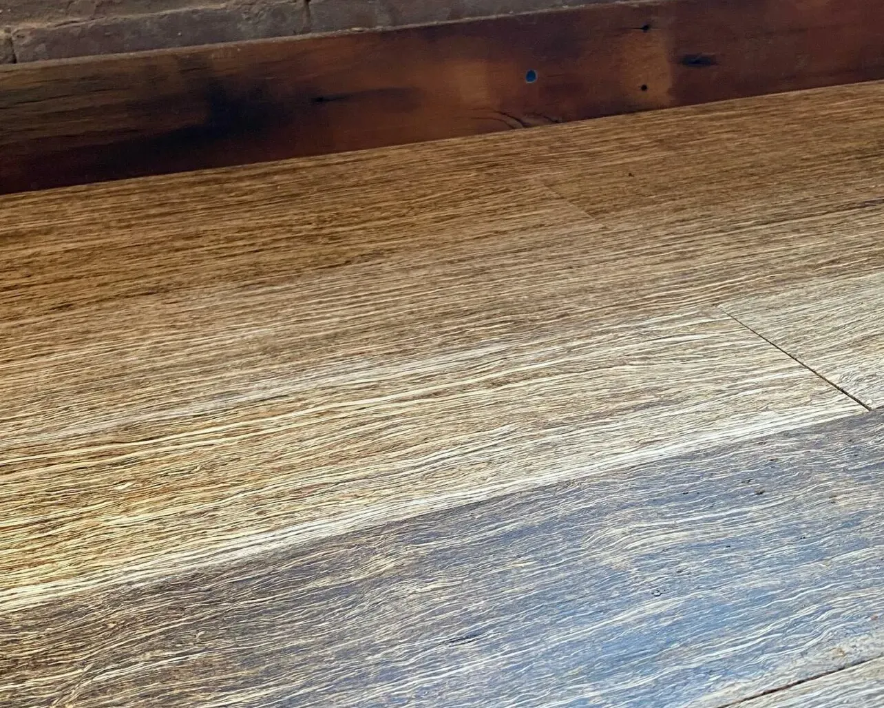 Close-up of textured wooden flooring installed against an exposed brick wall.