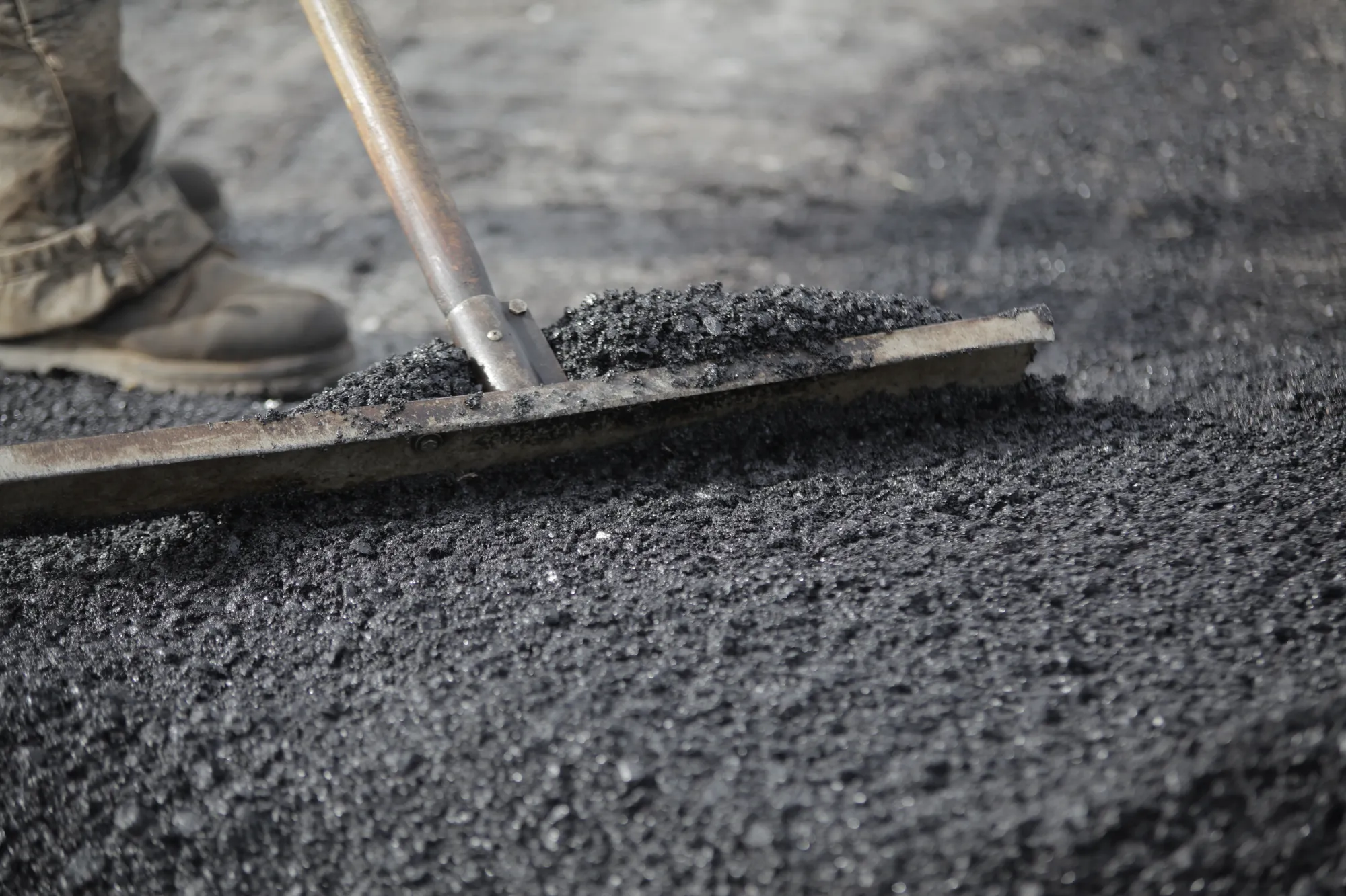 Worker using a rake to spread and level soy-based asphalt during paving.