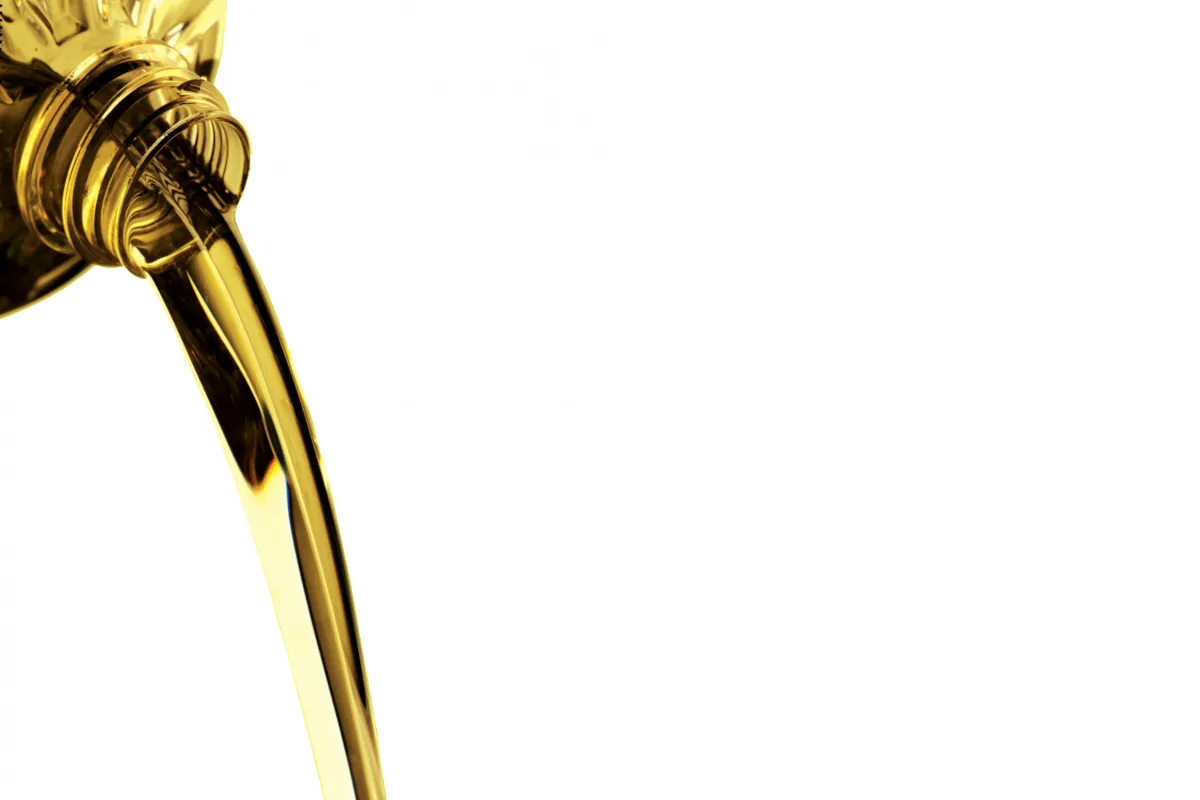 Golden cooking oil pouring from a bottle against a white background.