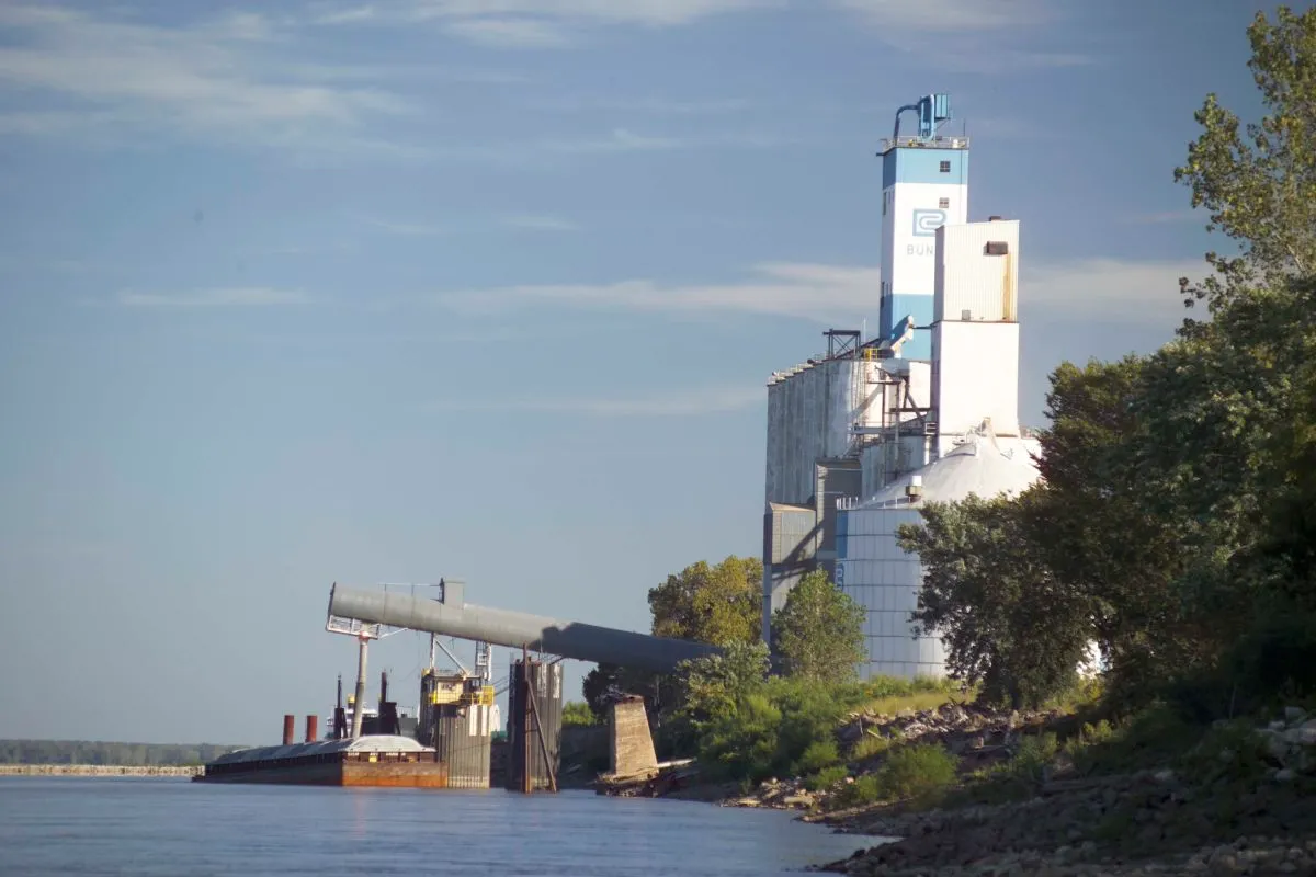 Grain elevator and storage facility along a river, with a barge positioned at the loading terminal for transporting agricultural commodities.