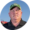 Portrait of farmer-leader Tom Frisch wearing a cap and collared shirt, photographed outdoors.