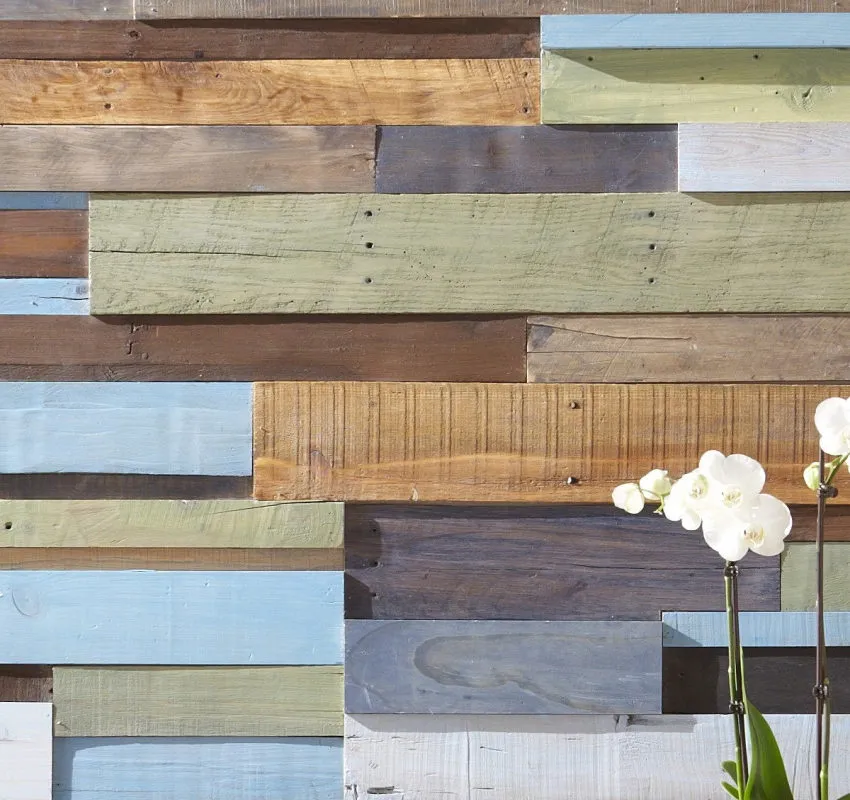 Wall made of wooden planks in a variety of colors and finishes, with white flowers in the foreground.