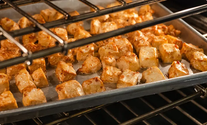 Tray of cubed tofu roasting in an oven, with golden-brown edges and a lightly crisped surface.